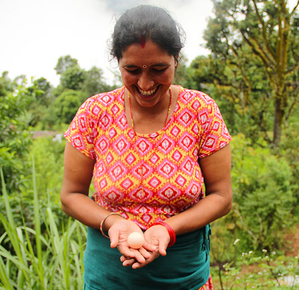 Photo of a woman smiling and holding an egg in a garden.