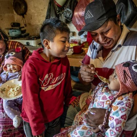 A mother and father feed their infant twins, while their young son looks on and tries to help.