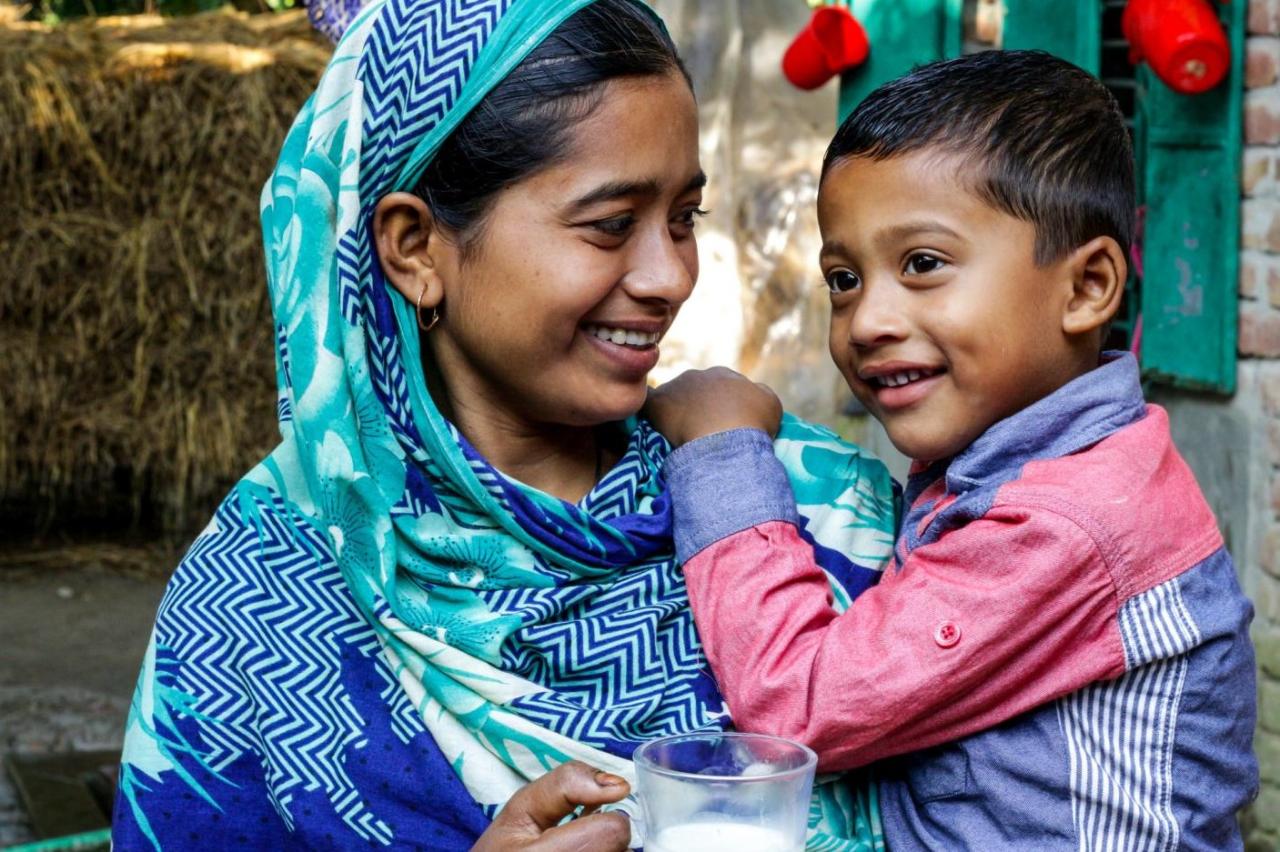 A mother is feeding milk to her son, which she is holding in her arms.