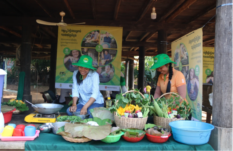 Two women preparing greens and veggies for meals in a local market
