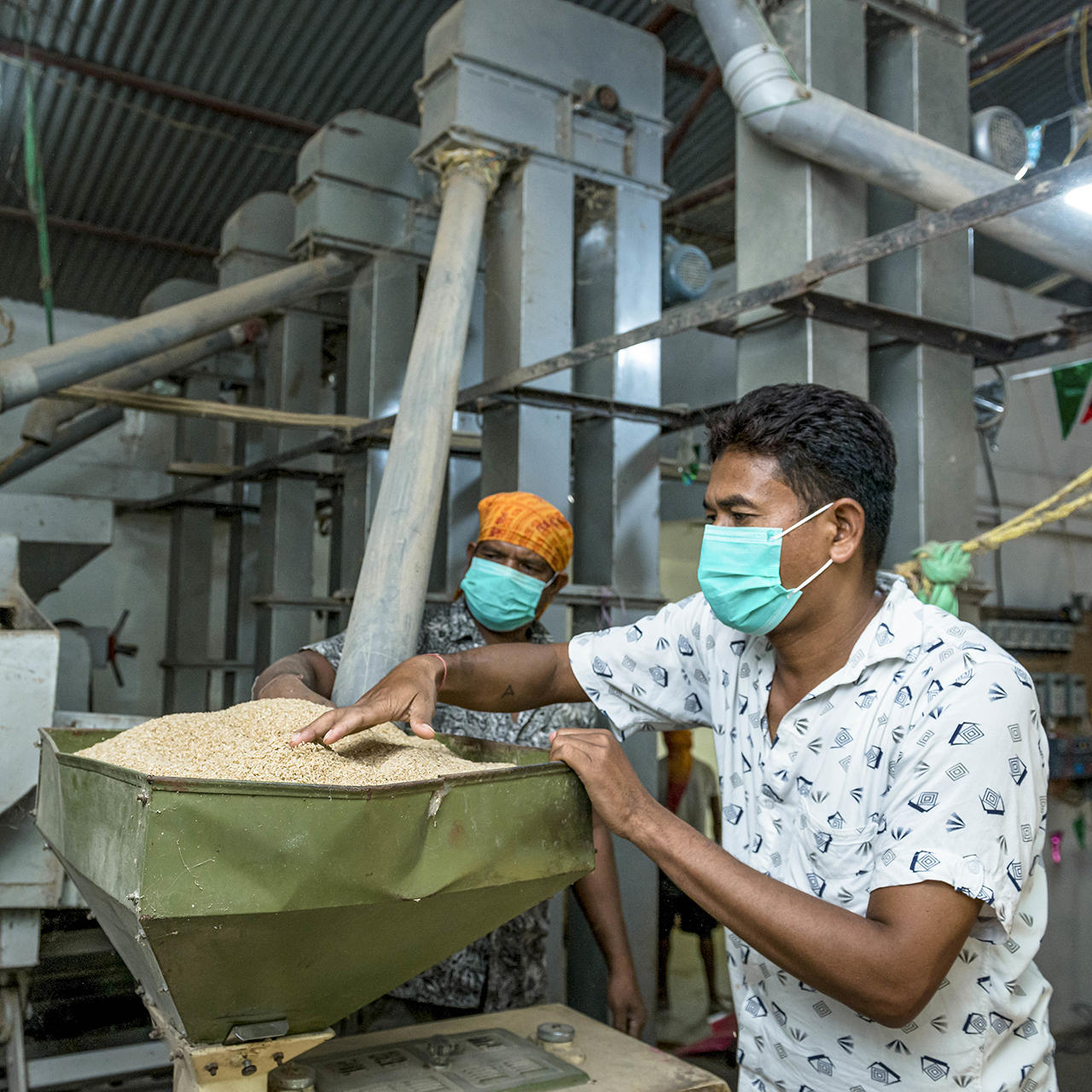 Two men working at a rice mill with masks on.