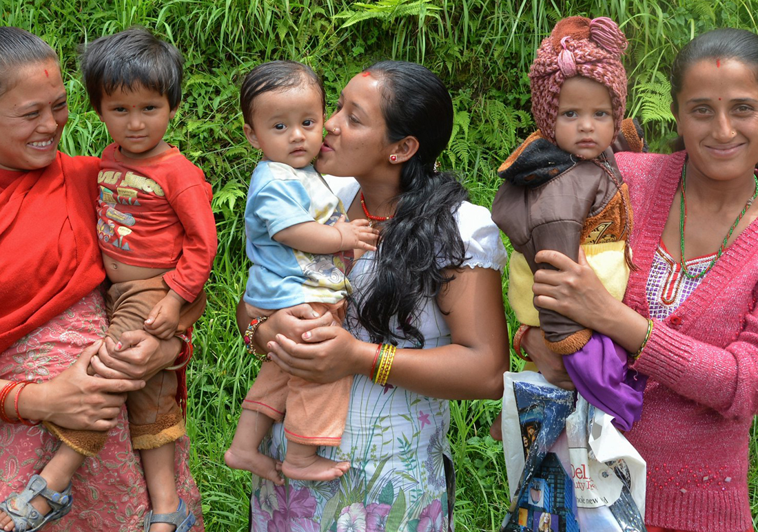 Three mothers holding their small children, while they are smiling outside