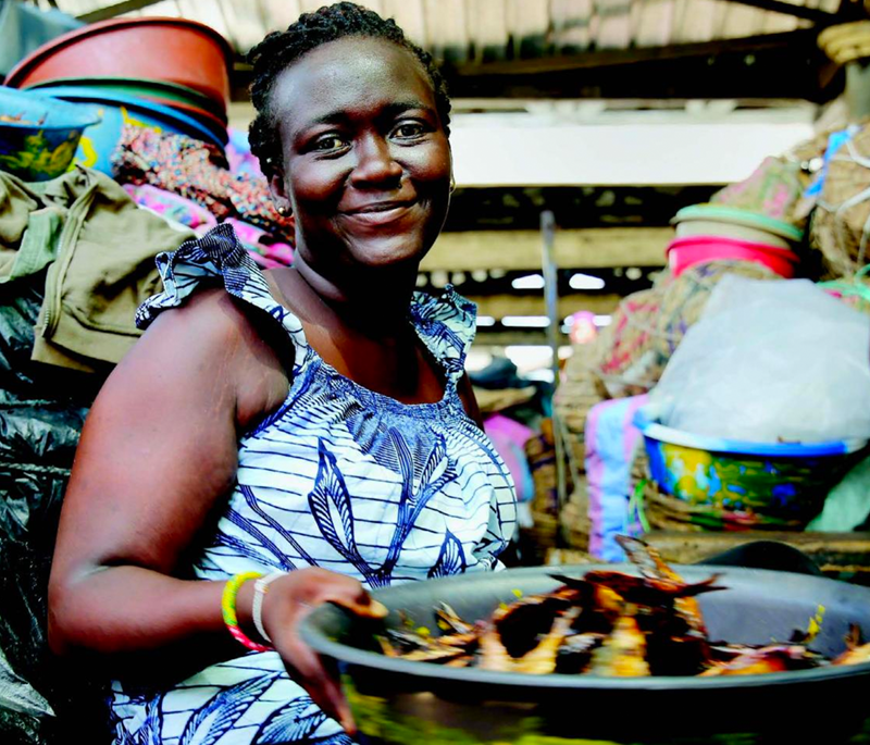 Women at a market holding a bowl of dried fish