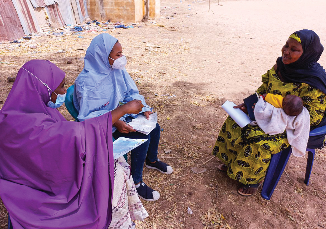 Photo of three woman chatting outside, one is holding a infant and the other two are CHWs