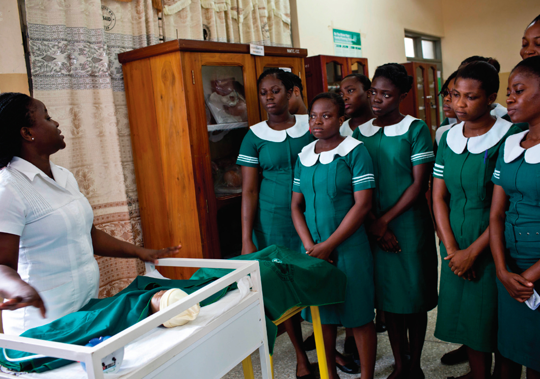 Group of health workers watching a trainer show them how to work with a newborn in a classroom.