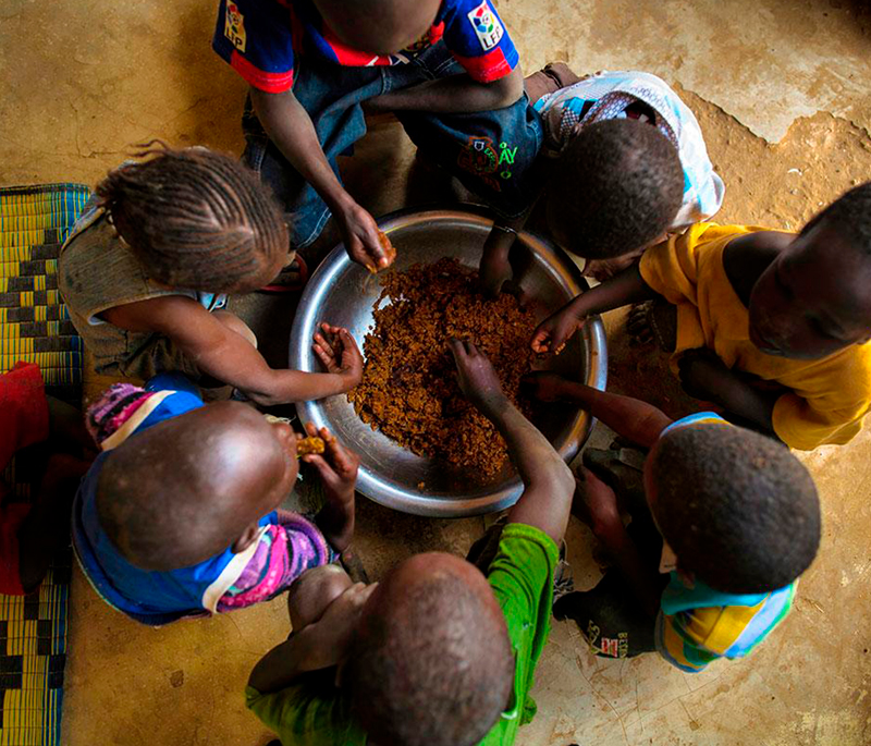 Seven children eating from a bowl on the floor (Source: Morgana Wingard, USAID).