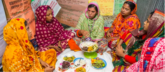 An extension worker from the Feed the Future Bangladesh Aquaculture and Nutrition Activity is demonstrating balanced and nutritious food to pregnant and lactating mother at a training session in Jashore, Bangladesh.