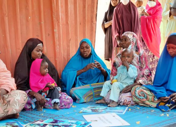 Group of women in Nigeria sit and hold their children on a mat