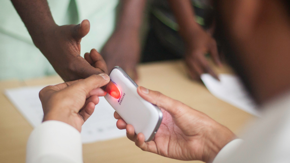 A health worker is using a smart phone light to screen a person for anemia by inspecting their finger.