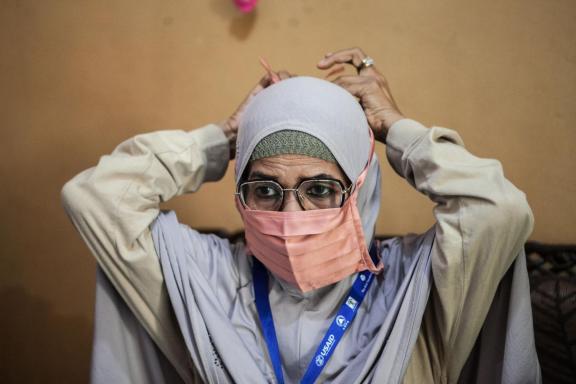A nurse wearing a head covering is tying a face mask.