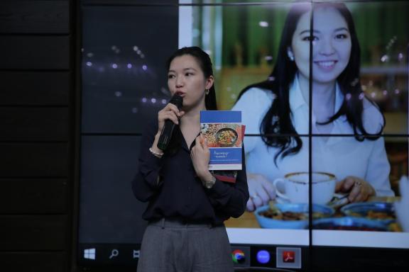 Photo of Zhanygul Sulaimanova presenting the USAID Advancing Nutrition Cookbook on stage