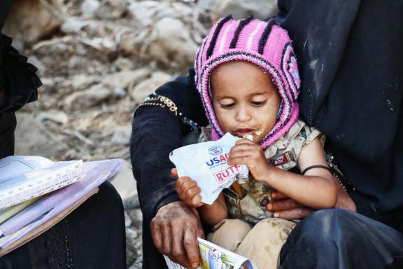 Photo of a small child in Yemen eating a ready-to-use therapeutic food bag.