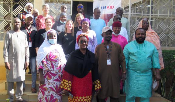 Group photo of USAID and partners outside, wearing traditional garb.