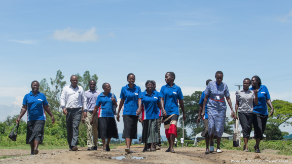 Group of health workers standing in a line, walking towards the camera, while outside on a nice day.