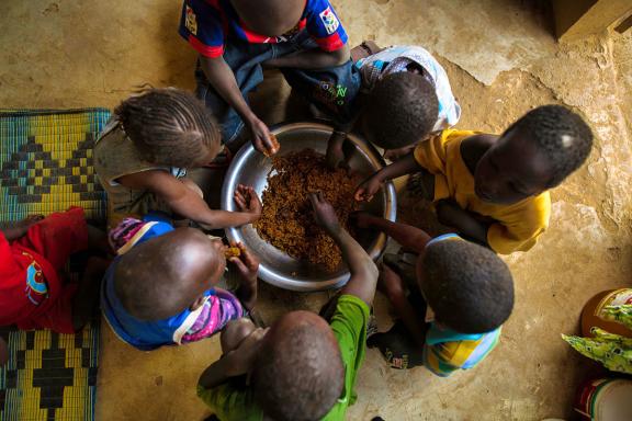 Seven children eating from a bowl on the floor (Source: Morgana Wingard, USAID)