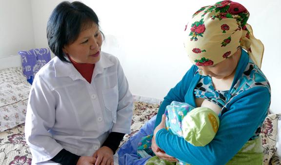 Mother breastfeeding a very young infant, at a clinic under the supervision of a health care professional. 