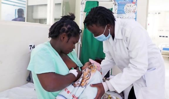 Mother in Kenyan hospital breastfeeding her newborn as a health practitioner shows her how to properly feed said newborn.