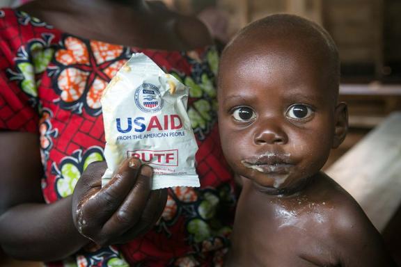 Infant eating while woman holds USAID bag