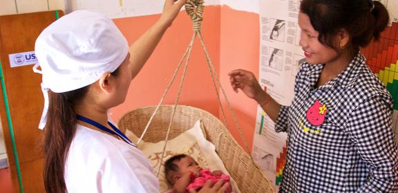 Health worker tracking a young child growth with a weighing basket, as the mother looks on.