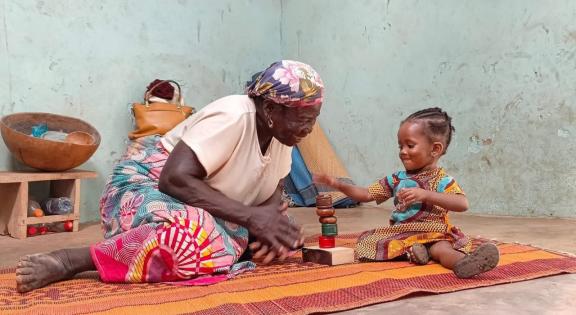 Ghanian grandmother playing with her grandchild on a mat on the floor with building blocks. 