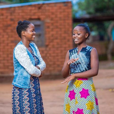 Two young women in Malawi are standing outdoors engaged in conversation.