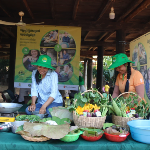 Two women preparing greens and veggies for meals in a local market