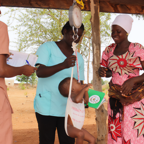 Two Ghanaian Health workers weighing a small child outside as the mother looks on.