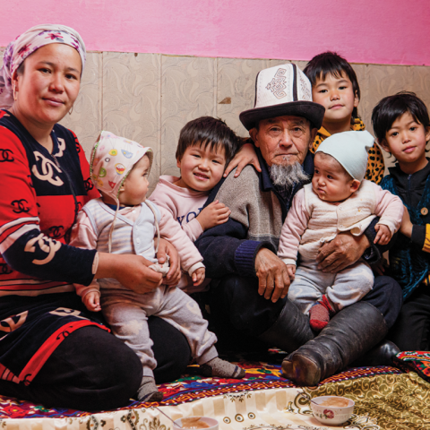 Grandmother and Grandfather in traditional Kyrgyz clothing with their four grandchildren of various ages, in a group photo.
