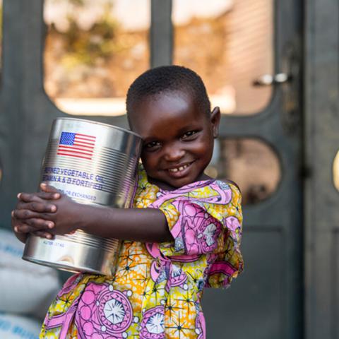 Photo showing a small child holding a can of food provided food by USAID Africa after thousands displaced from Goma after Volcano eruption.