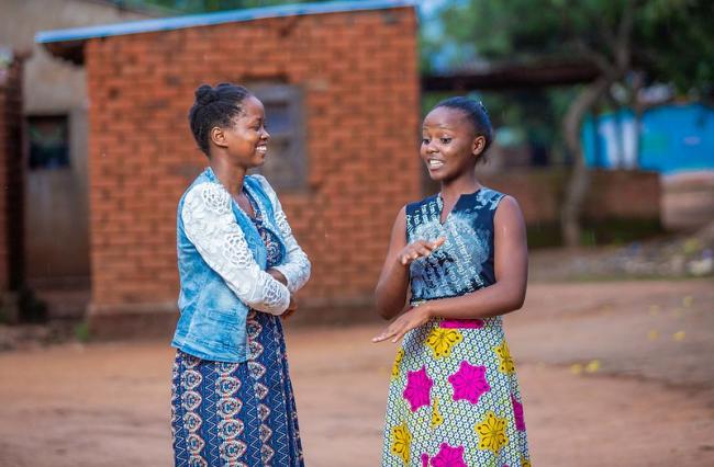 Two young women in Malawi are standing outdoors engaged in conversation.