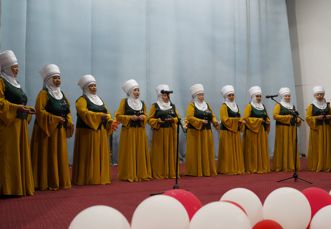 A group Kyrgyz women in folk-outfits on stage and singing at the event.