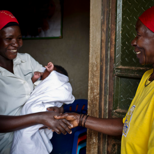 Women shaking hands, while one woman holds her child