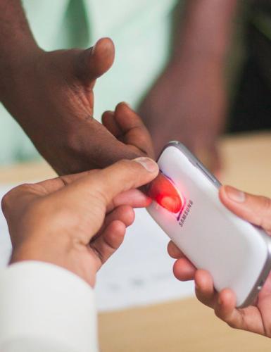 A health worker is using a smart phone light to screen a person for anemia by inspecting their finger. Photo Credit: Jessie Bryson, USAID/Tanzania