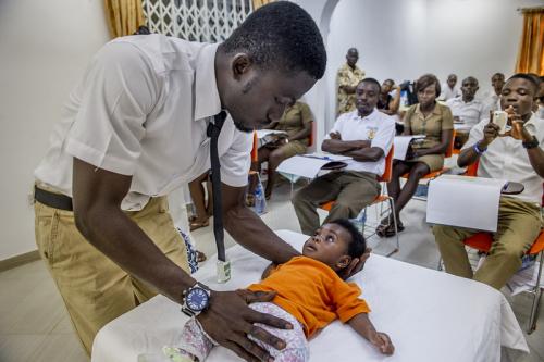 Health provider examining a small infant in front of a classroom of health students.