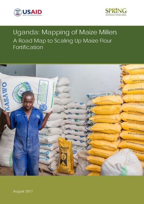 <an carrying a sack; piles of other sacks are behind him. Caption: "Maize mill employee Haruna Ssemakula carries a sack of maize flour to a waiting truck. Photo Credit: SPRING/Uganda.