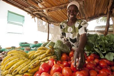 Woman standing in front of her fruit and vegetable stand, at a local outdoor market.
